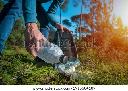 Man cleaning-up the forest of plastic garbage. Nature cleaning. Volunteer picking up a plastic bottle in the woods. Green and clean nature. Plastic awareness activism and ecology concept