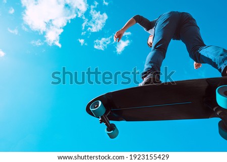 Skater in action. Man making a trick on a longboard outdoors on sunny summer day. Blue sky background. Concept of extreme sport active lifestyle