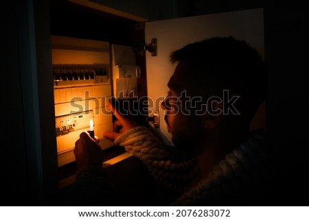 Man with lighter in total darkness investigating fuse box or electric switchboard at home during power outage. Blackout, no electricity concept ストックフォト © 