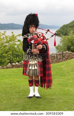 URQUHART CASTLE, SCOTLAND, UK - CIRCA AUGUST 2015: Scottish bagpiper dressed in traditional red and black tartan dress