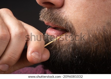 Close up bearded man clean teeth from food stuck her teeth with toothpick after breakfast, lunch, dinner. Rude behavior. Uncultured and impolite habit Foto stock © 