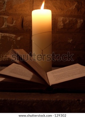 lit candle in the dark with a bible and cross round the candle