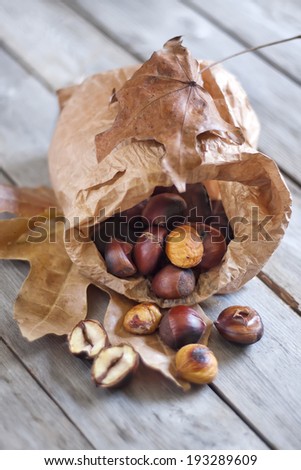 Roasted chestnut in a paper bag on old wooden table.