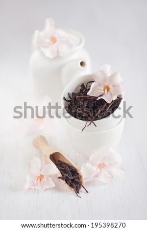 Oolong tea in a scoop, cups and teapot with light rose rhododendron flowers.