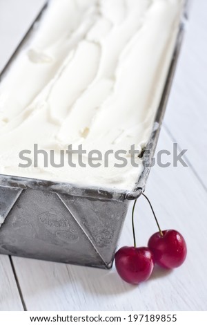 Homemade vanilla ice cream in frozen metallic container with ripe red cherry. Selective focus.