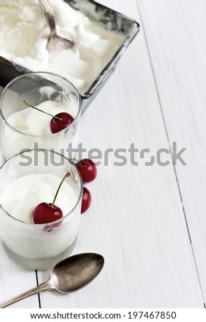 Homemade vanilla ice cream in frozen metallic container and glasses with ripe red cherry. Selective focus. Copy space background.