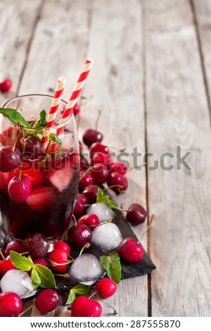 Cherry juice with ice cubes, mint leaves and ripe sweet cherry. Copy space background.