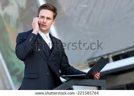 Good job on the mobile phone. Confident and motivated businessman is talking on a cell phone, while working with laptop