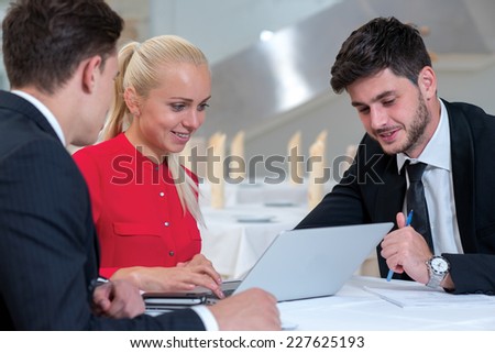Meeting business clients. Two successful and confident businessmen and one stylish businesswoman are sitting at the table with laptop and discussing the business project start