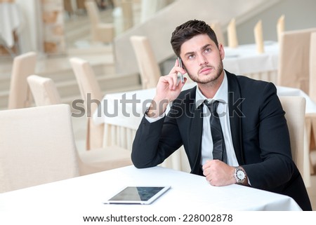 Good job with the mobile phone. Young and motivated businessman is sitting at the table with tablet and mobile phone and thinking about business offer