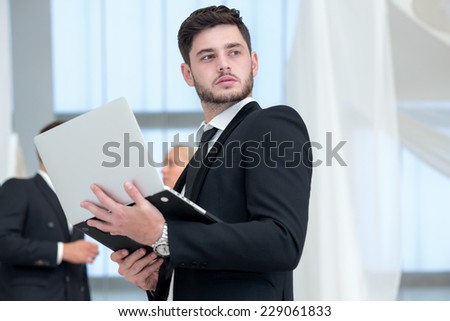 Thinking about future projects. Young and motivated businessman is standing with laptop and thinking about important business stuff
