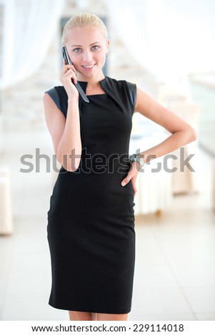 Good business stuff on the phone. Young and pretty businesswoman is standing with the mobile phone and discussing the business project issues