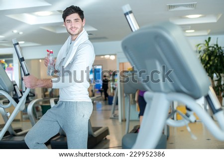 Portrait of young and handsome guy standing with bottle of water and towel on his neck