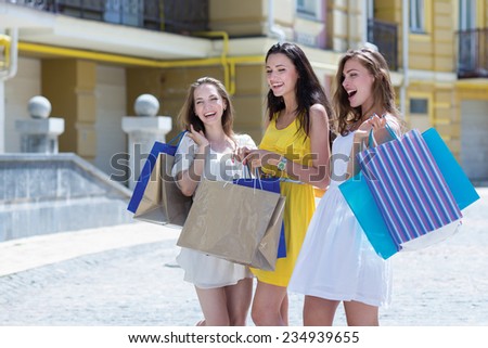 Awesome shopping sales proposition. Three young and attractive women are standing on the street with shopping bags. Girls are smiling and looking forward happily, because of their purchases