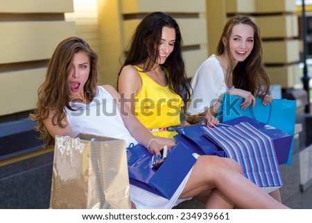 Look at this price on the dress. Three young and attractive women are sitting with shopping bags. One of the girls is astonished about the special offer in a shop