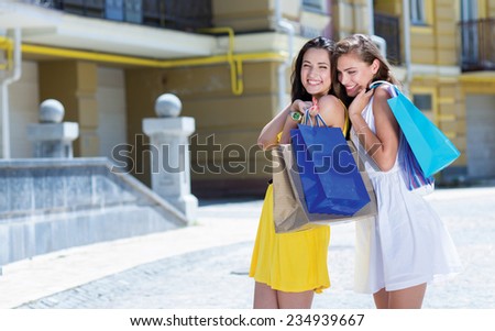 Happy about great sales proposition while shopping. Two attractive young women are standing on the street with shopping bags. Girls are happy and smiling