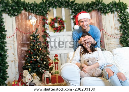 Christmas surprise. Couple in love is in festive Christmas decorated living room. Man is ready to give New Year present to his girlfriend.