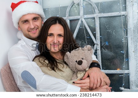 Merry Christmas and Happy New Year. Young beautiful couple in love is sitting together and smiling just before Christmas. Winter window is on the background
