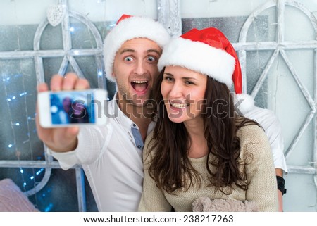 Christmas selfie.Young beautiful couple in love is making selfie in New Year decorated living room. Winter window is on the background