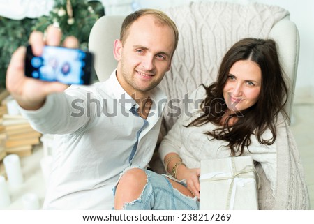 Christmas selfie. Couple in love is in festive Christmas decorated living room is making selfie on mobile phone just before happy New Year time