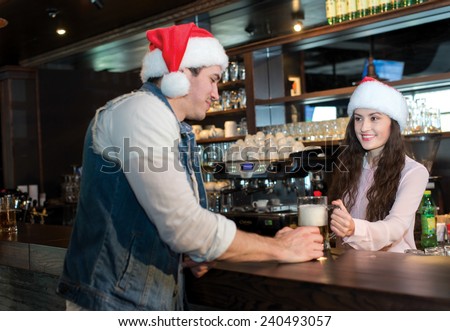 New Year in a bar with beer. Girl bartender is giving Christmas beer to young man. Both are wearing New Year Santa Claus hats