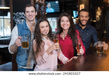Friends are having fun with beer. Four best friends are standing in a pub and drinking beer with smiles