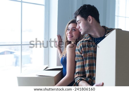 Entering new house. Young and beautiful couple is moving to new apartment surrounded with plenty of cardboard boxes. Girl and man are looking on each other