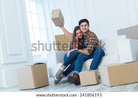 Moving new flat with fun and excitement. Young and beautiful couple is moving to new apartment surrounded with plenty of cardboard boxes. Both are smiling