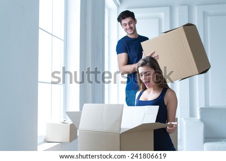 Moving new house. Young and beautiful girl is opening cardboard boxes, while moving new flat with her husband