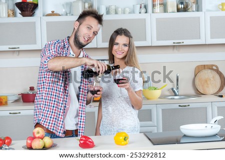 Some wine on the kitchen. Young and beautiful couple in love is preparing food on the kitchen, while pouring wine in glasses. Diet. Dieting. Healthy vegetarian food