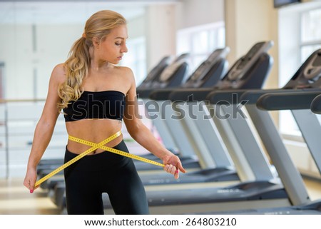 Perfect sport shape. Portrait of young and pretty athlete girl in a gym. She is metering her body and enjoys the proper sport result