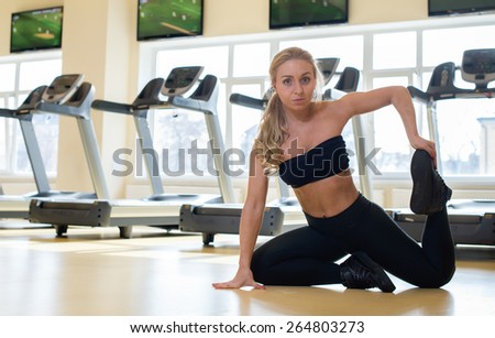 Proper warm up. Portrait of young and pretty athlete girl in a gym. She is doing warm up near the line of treadmills