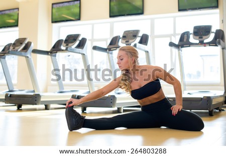 Proper warm up. Portrait of young and pretty athlete girl in a gym. She is doing warm up near the line of treadmills