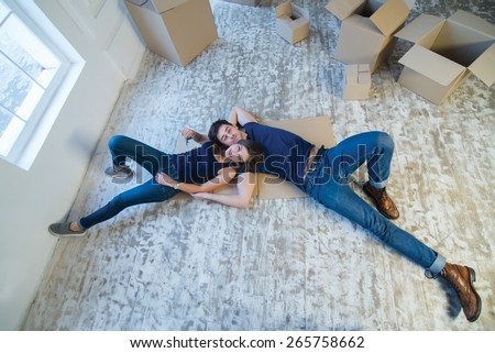 Moving new flat with fun and excitement. Young and beautiful couple is moving to new apartment surrounded with plenty of cardboard boxes. Both are laying on the floor