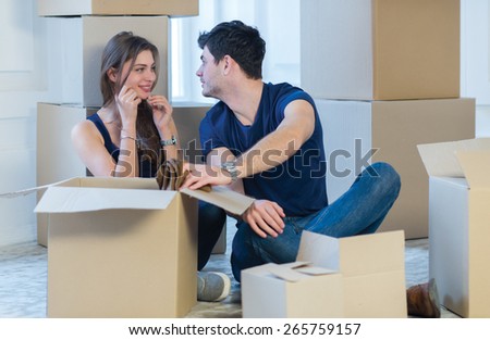 Moving new flat with fun and excitement. Young and beautiful couple is moving to new apartment surrounded with plenty of cardboard boxes. Both are sitting on  floor and dreaming about new cozy house