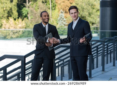 Excellent business agreement. Two confident and motivated businessmen are shaking hands. Both are wearing formal suits. Outdoor business concept