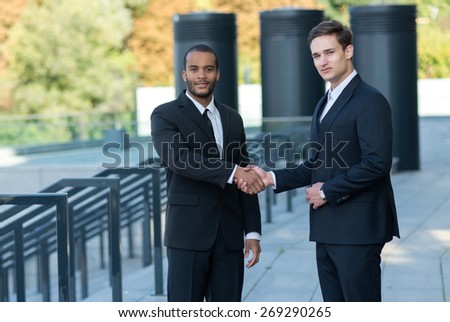 Proper business agreement. Two confident and motivated businessmen are shaking hands. Both are wearing formal suits. Outdoor business concept