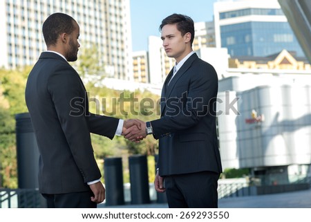 Proper business agreement. Two confident and motivated businessmen are shaking hands. Both are wearing formal suits. Outdoor business concept