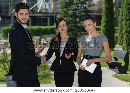 Perfect business relationship. Three confident and motivated business partners are discussing future business details and shaking hands. All are wearing formal suits. Outdoor business concept