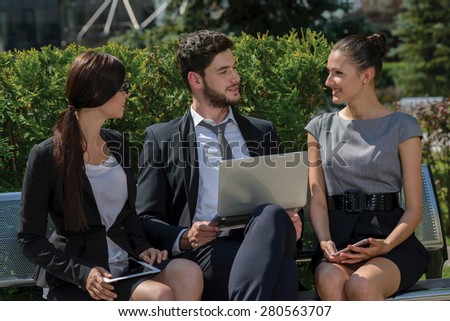 Working on successful project.  Three confident and motivated business partners are discussing business details of current projects. All are wearing formal suits. Outdoor business concept