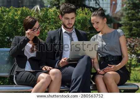 Working on successful project.  Three confident and motivated business partners are discussing business details of current projects. All are wearing formal suits. Outdoor business concept