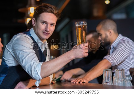 Beer evening in a pub. Portrait of young successful and handsome man drinking beer in a pub with his friends. Beer glasses.  Beer football pub concept.