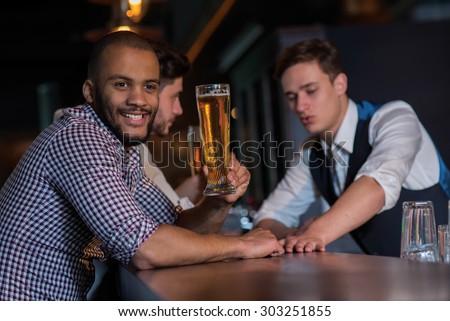 Beer evening in a pub. Portrait of young successful and handsome man drinking beer in a pub with his friends. Beer glasses.  Beer football pub concept.