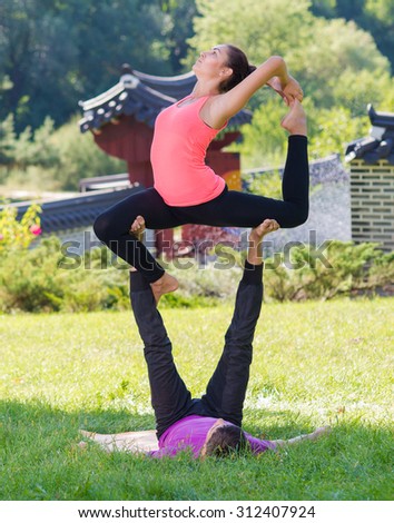 Perfect acroyoga. Beautiful young couple is balancing doing acro-yoga. Pair yoga concept. Yoga flexibility outdoor class workout