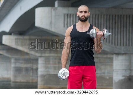 Professional fitness athlete trainer. Muscular male sportsman is training himself with dumbbells. Outdoors fitness sport concept. Street workout