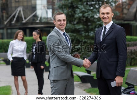 Proper business agreement. Group of confident and motivated business partners at work, both are shaking hands. Both men are wearing formal suits. Outdoor business concept
