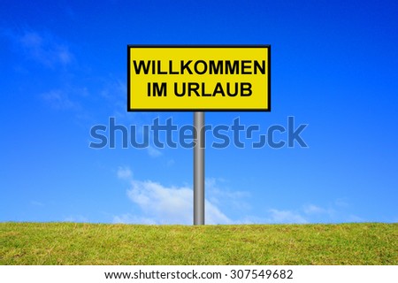 Yellow signpost on green grass showing welcome holidays in german language in front of blue sky