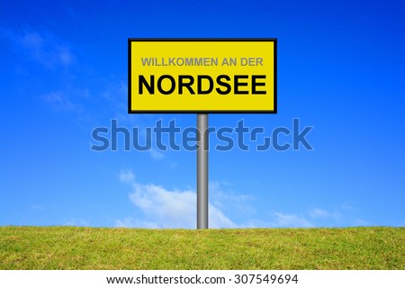 Yellow signpost on green grass showing welcome at the north sea in german language in front of blue sky