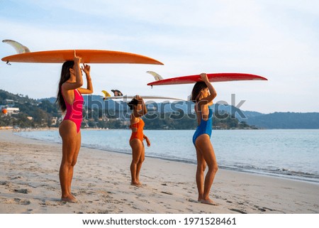 Portrait group of Asian woman girl friends in swimwear holding surfboard standing on the beach together at summer sunset. Female friendship enjoy outdoor activity lifestyle play extreme sports surfing