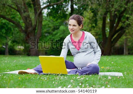 Beautiful pregnant woman with laptop in the park